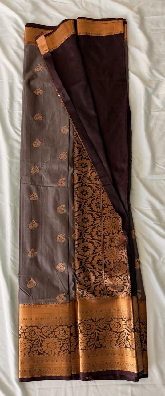 Warm taupe-brown Kanchipuram silk saree with scattered gold butta motifs, floral and paisley patterns, and wide gold-striped border with dark brown and black ornate scrollwork