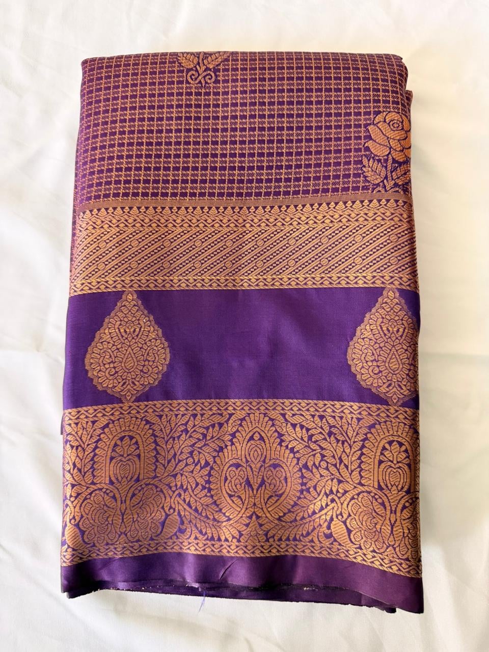 Deep wine purple Kanchipuram silk saree with floral checks and ornate gold border, folded detail view