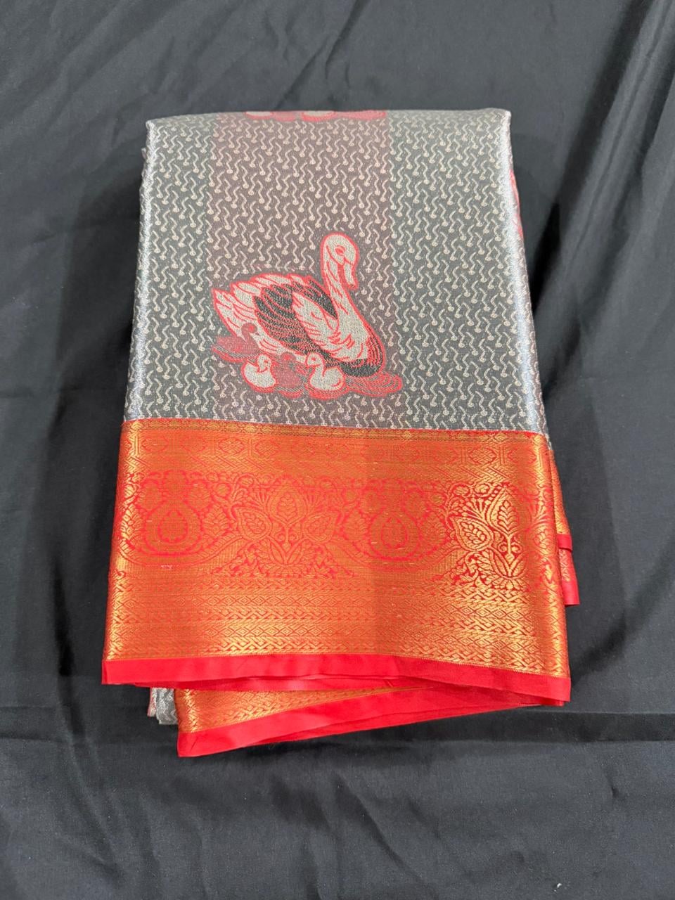 Silver grey Kanchipuram silk saree with peacock motifs and red-gold ornamental border, folded detail view